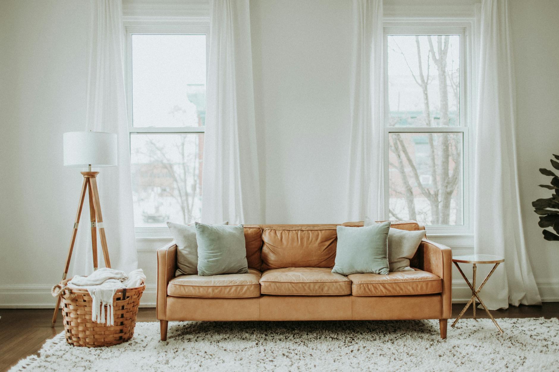 A living room with a brown sofa and two sash windows with curtains