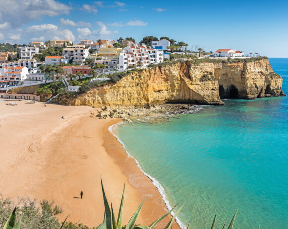 Whitewashed houses on a cliff above a golden beach in the Algarve