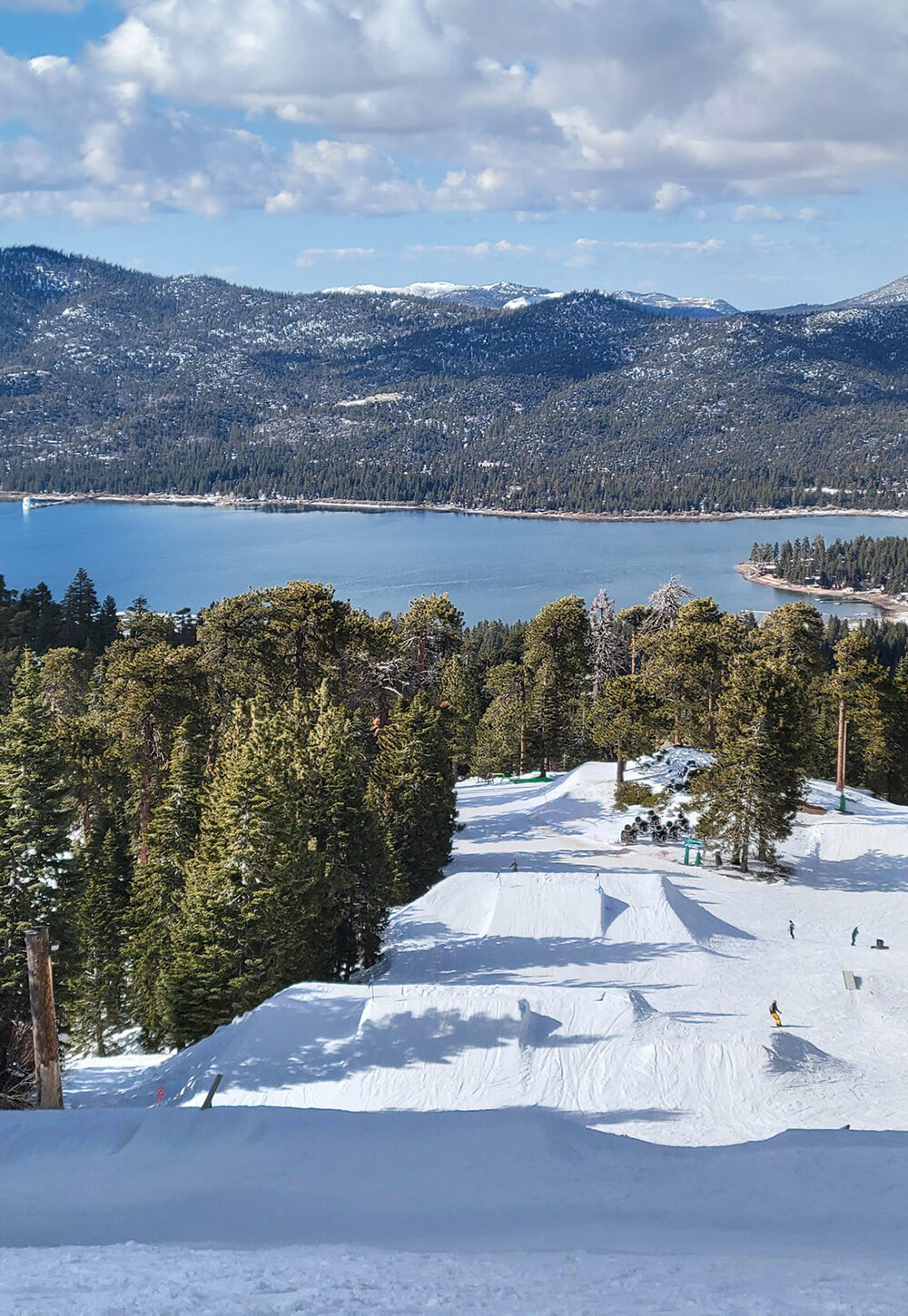 A fresh ski slope between wooded trees heading down towards a lake