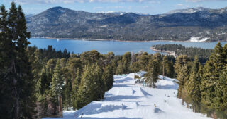 A fresh ski slope between wooded trees heading down towards a lake