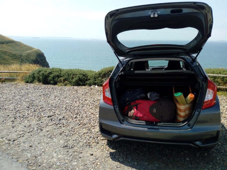 Car parked overlooking the sea with the boot open and luggage inside