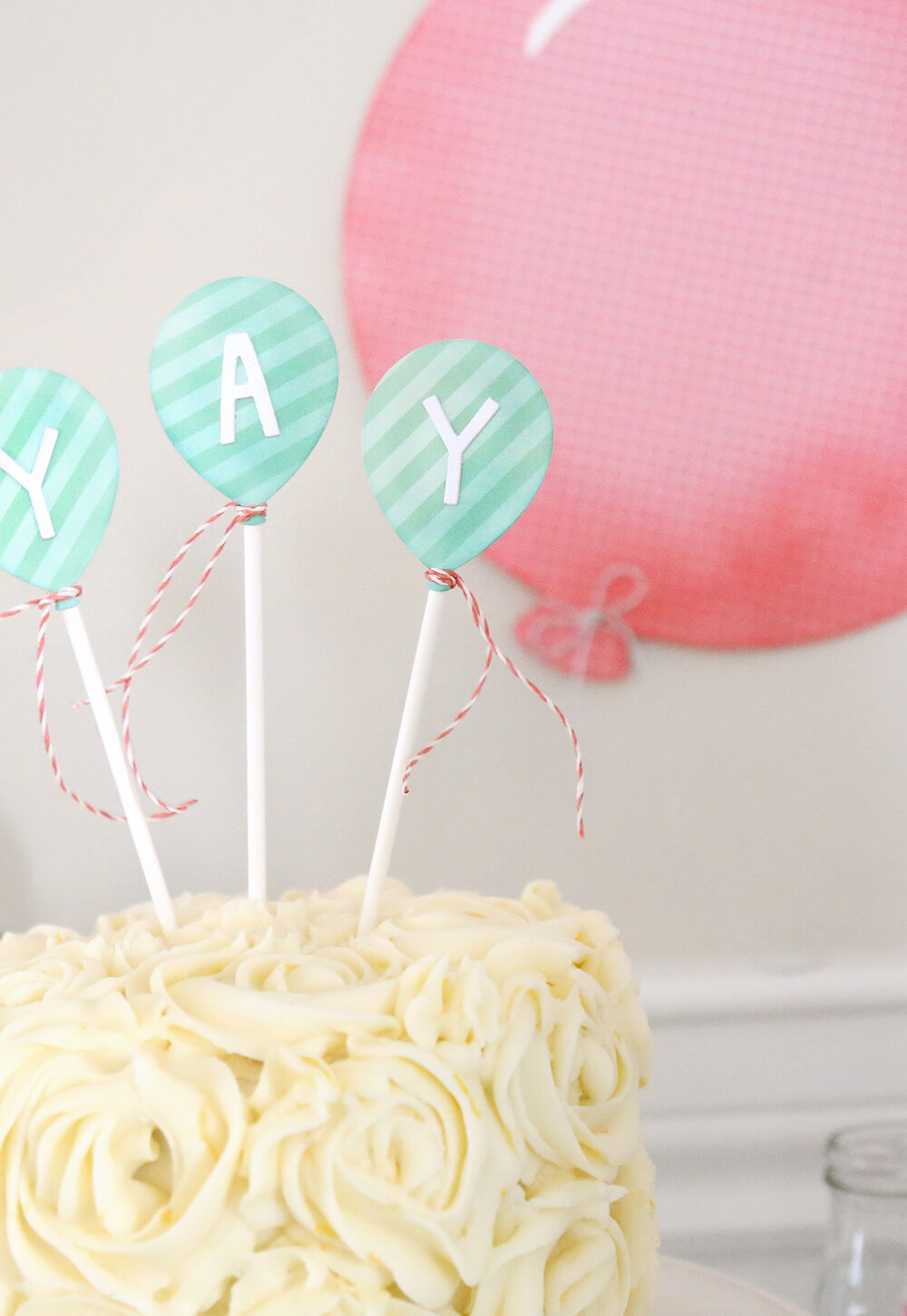 Birthday cake with balloon cards sticking out of it that say "yay"